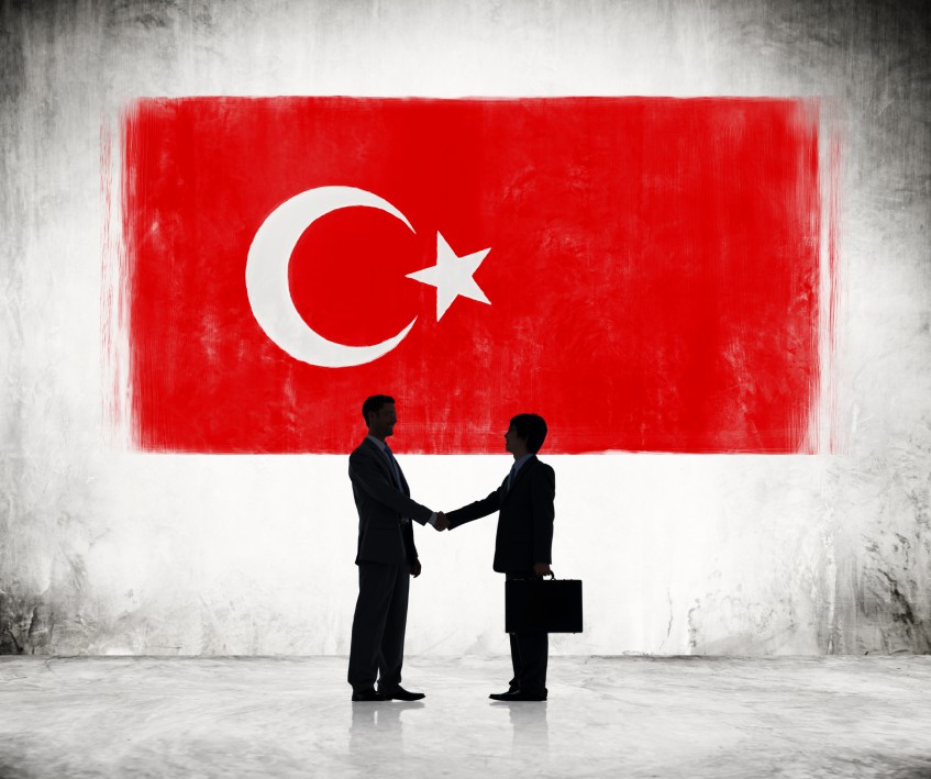 Two Businessmen Shaking Hands With Turkish Flag As A Background