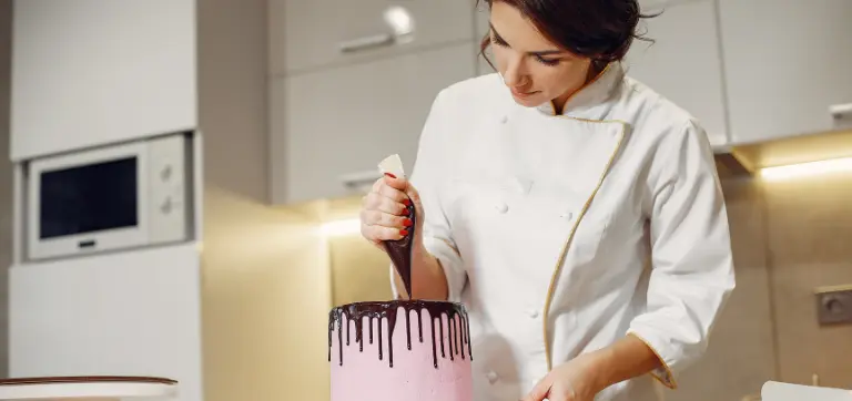 Chef autónoma decorando un pastel de goteo rosa con glaseado en un entorno de cocina.