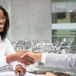 Dos profesionales se dan la mano sobre una mesa en una cafetería de oficina moderna.